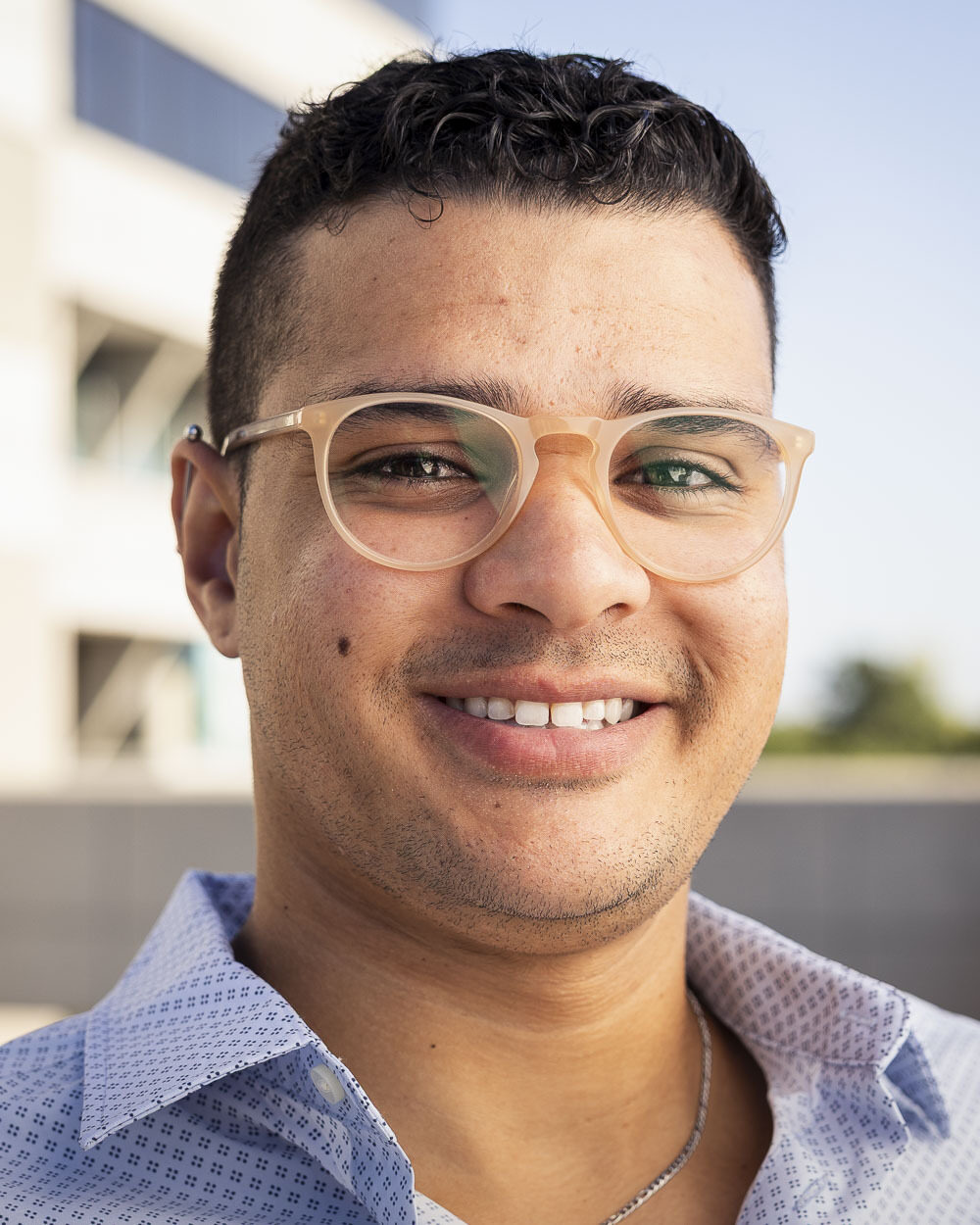 Portrait of Davi Mourao, a man with short dark hair wearing glasses and a blue patterned shirt.