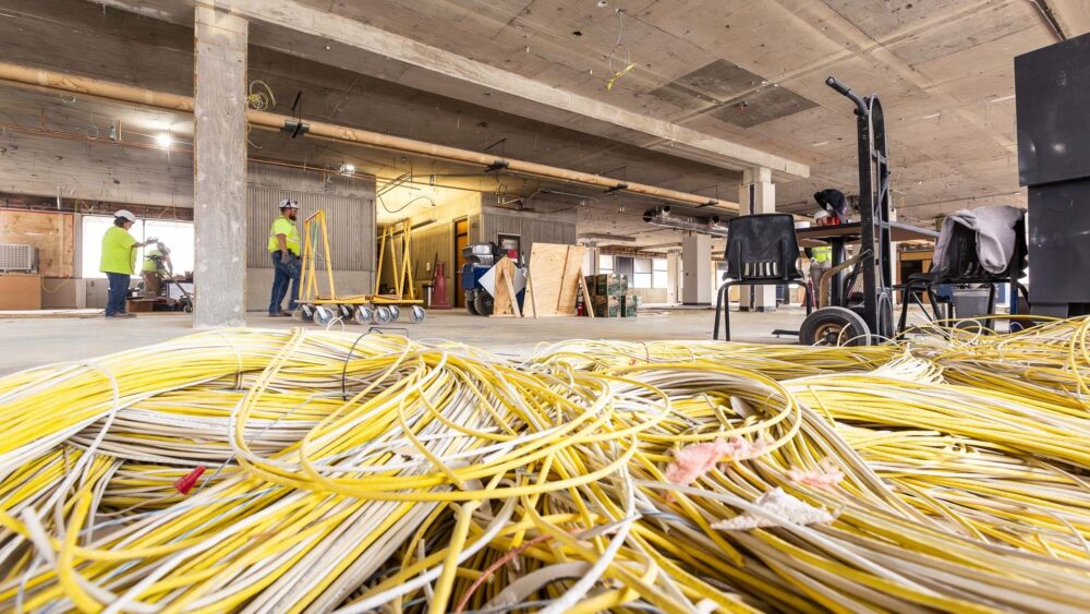 A pile of yellow and white cables in the foreground with construction works walking through the background.