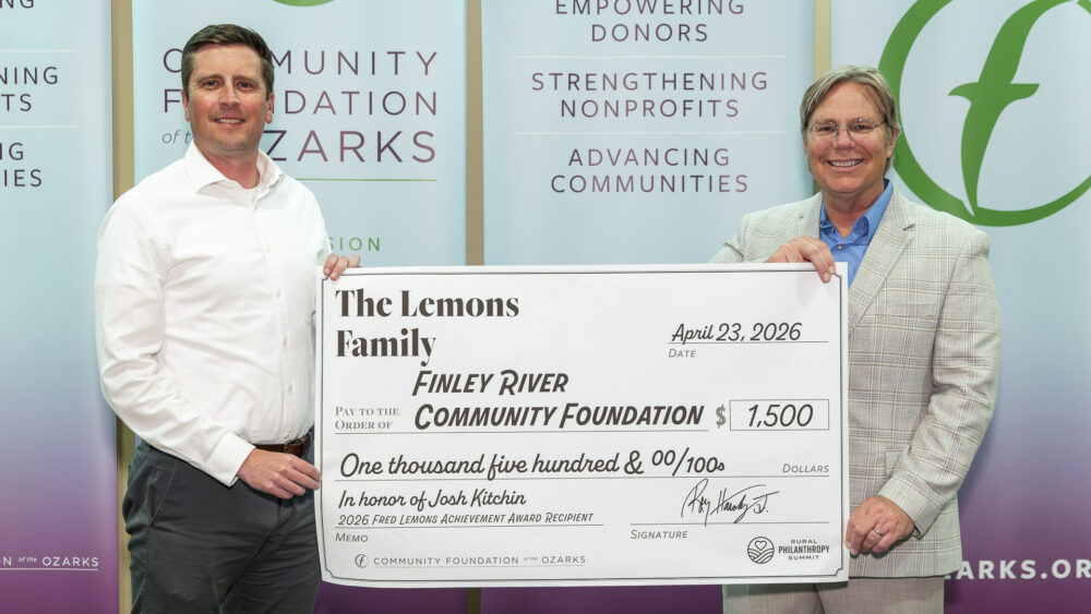 Two men — Josh Kitchin and Joe Kammerer — pose holding a large ceremonial check for $1,500 payable to the Finley River Community Foundation from the Lemons Family. The check references the 2026 Fred Lemons Achievement Award, with Community Foundation of the Ozarks banners behind them.