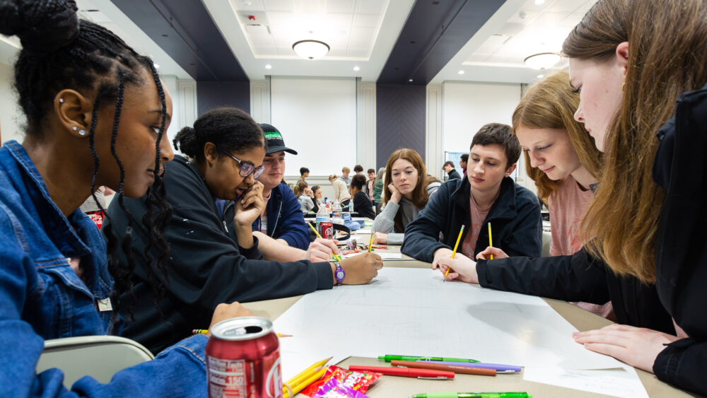 Seven high school students crowd around a large piece of paper to explore the idea of placemaking.