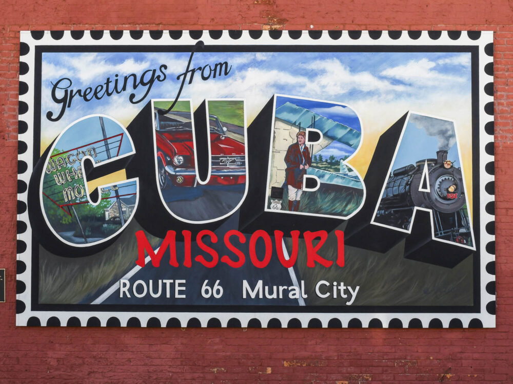 A vibrant mural styled like a giant "Greetings from Cuba, Missouri" postcard. The letters "CUBA" contain smaller paintings of a classic red car, a train, and local landmarks.