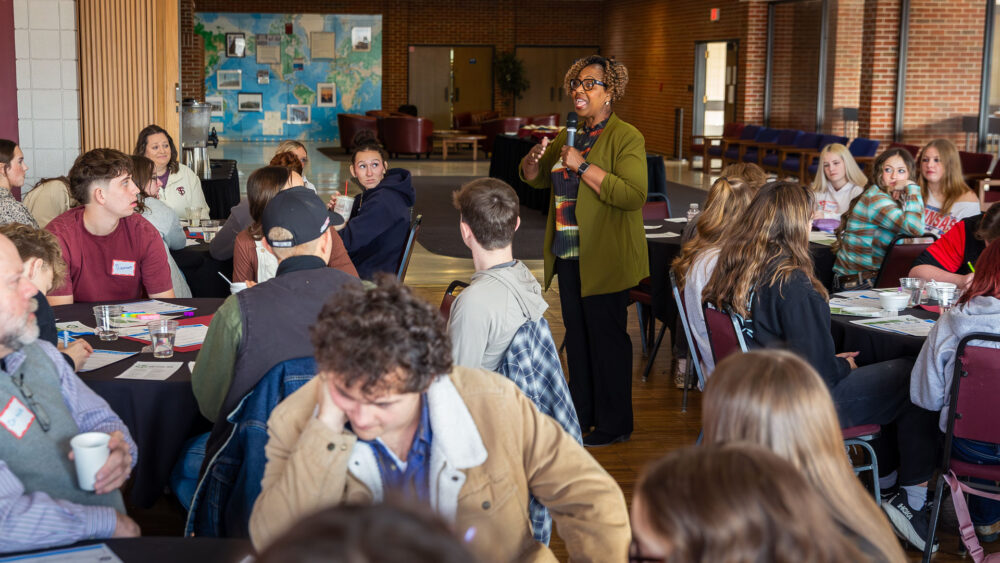 A woman speaks to an audience of high school students and teachers.