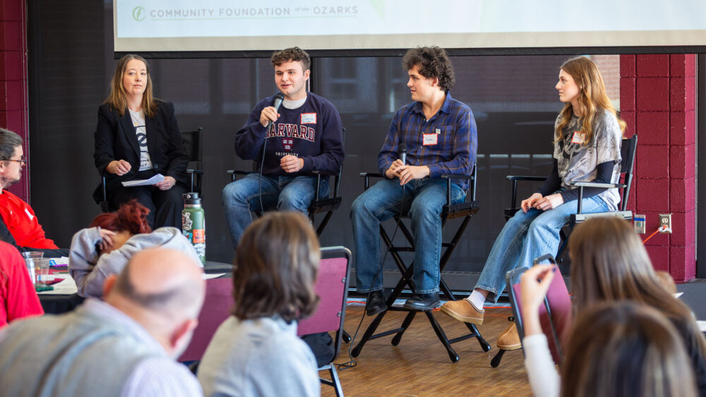 A woman and three young people sit on director's chairs in front of an audience.