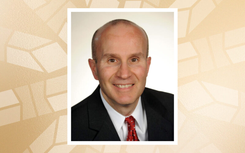 Portrait of Hank Molinengo, a man wearing a dark suit and red tie, framed against a gold geometric patterned background.