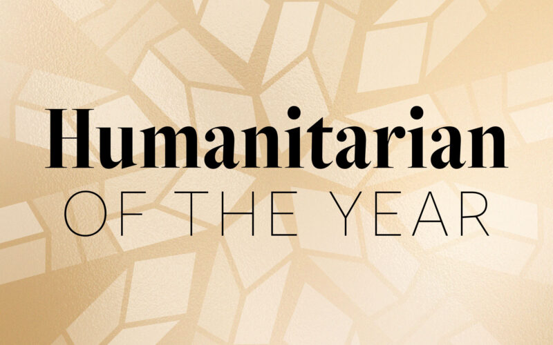 Black text reading "Humanitarian of the Year" appears on a gold background with a light geometric pattern resembling a crystal award.