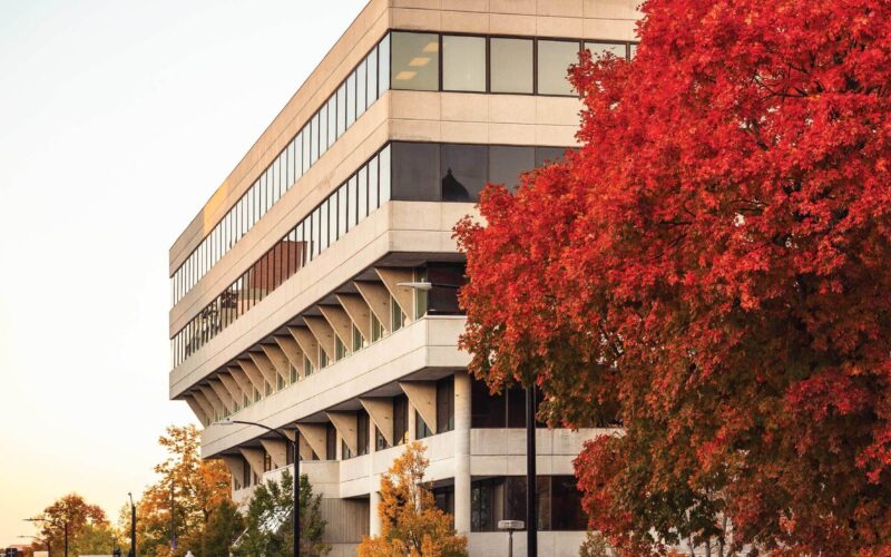 A brutalist-style building at sunset in the fall, with a tree of bright red leaves in the foreground.