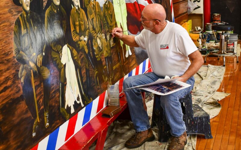Picture of a man painting a large mural depicting soldiers from World War I, a bald eagle and an American flag.