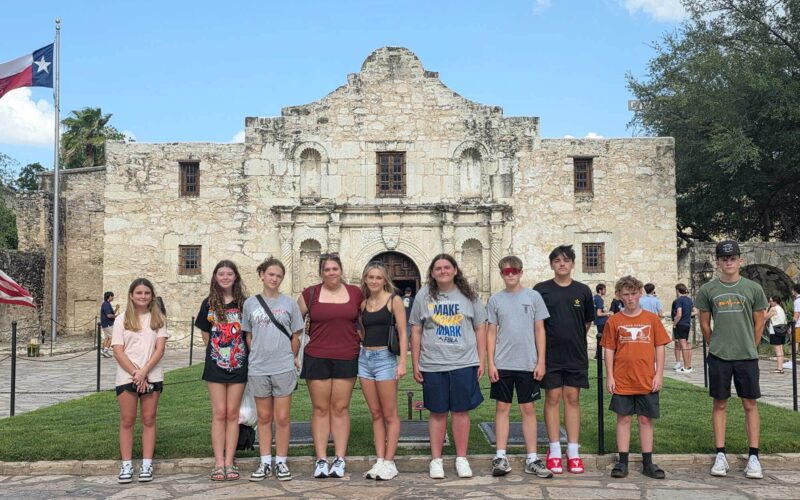 A group of 10 young people poses in front of the Alamo in San Antonio, Texas.