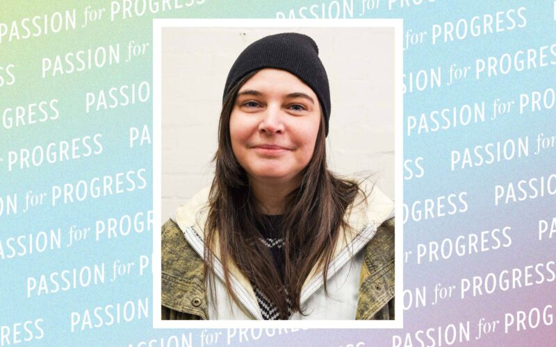 A headshot of Re Baker-Dietz, a woman with long dark hair wearing a black beanie and a green utility jacket. The background is a light blue and purple gradient with the repeating words "PASSION for PROGRESS."