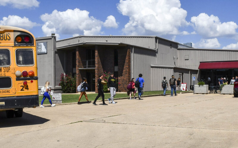 Students carrying backpacks walk toward the Southern Missouri Technical Institute from a parked yellow school bus on a sunny day in West Plains, Missouri.