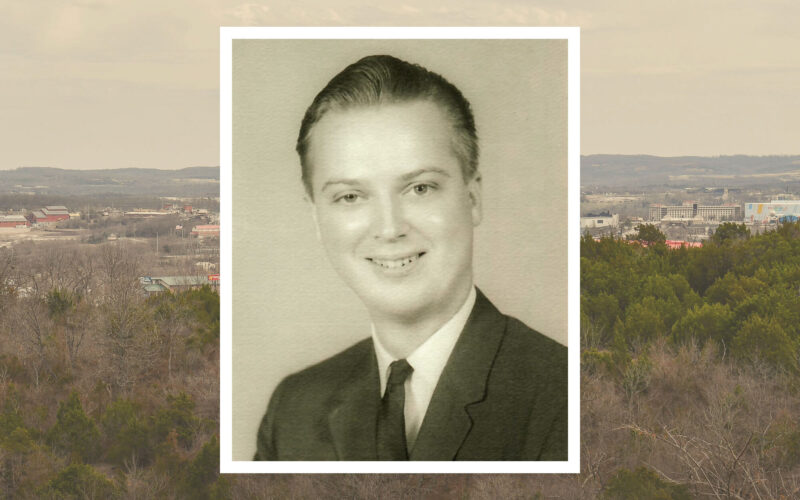 The background shows a panoramic shot of Branson, Missouri, in winter with a photo in the center. The photo is a black-and-white portrait of a man, smiling and wearing a suit and tie.