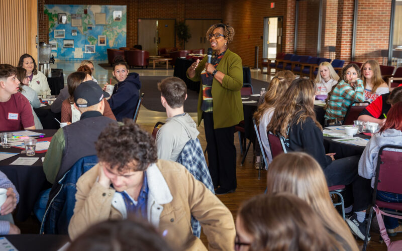 A woman speaks to an audience of high school students and teachers.