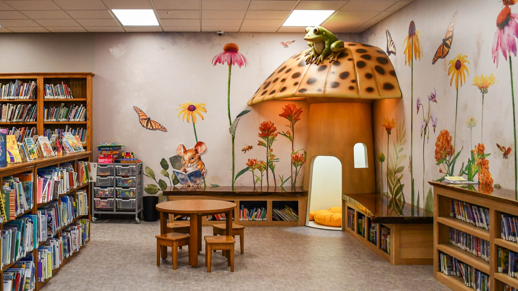 The new children's section of the Houston, Missouri, library features shelves of books, a mushroom-shaped cubby booth in the corner, and a mural of butterflies and flowers.