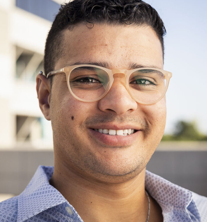Portrait of Davi Mourao, a man with short dark hair wearing glasses and a blue patterned shirt.