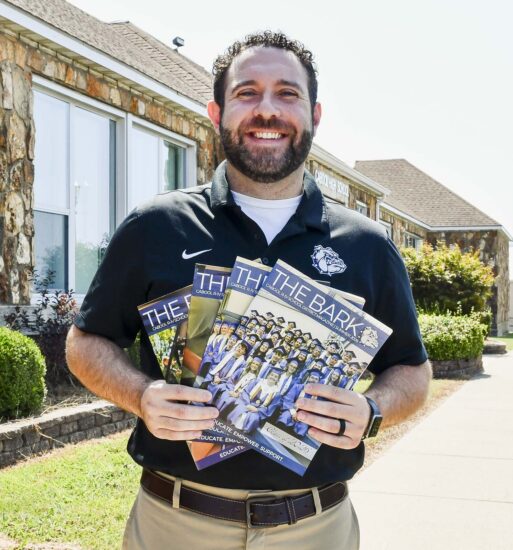 Nathan Christeson stands outside a school building in Cabool, Missouri, holding several issues of The Bark, the school's student-led magazine.