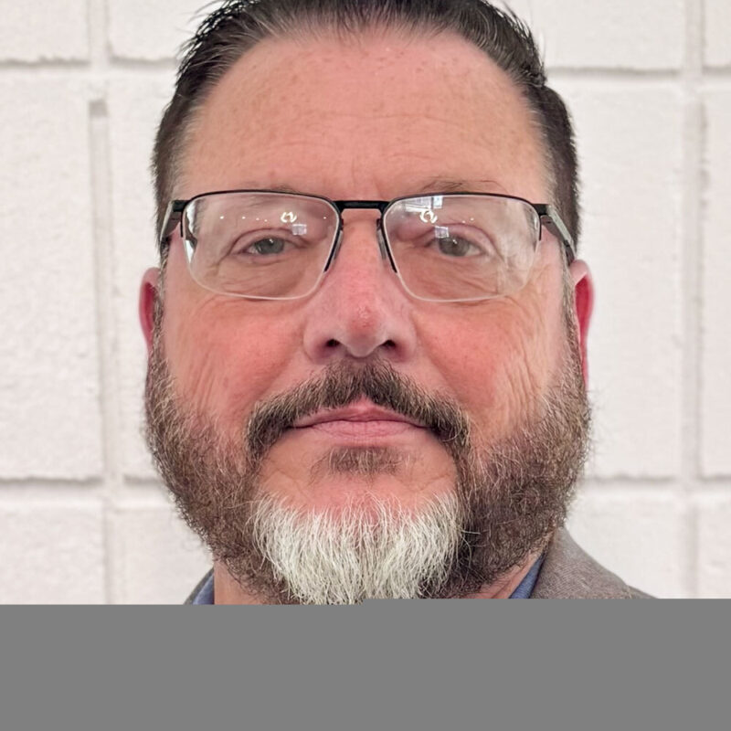 Portrait of Russell French, a man with short brown hair and beard wearing glasses, a blue shirt and gray blazer.